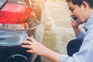 man calling insurance company next to car claiming his car crash damaged road accident